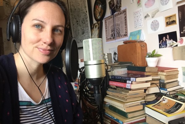 Amy Tsilemanis in her home studio with a microphone and surrounded by books